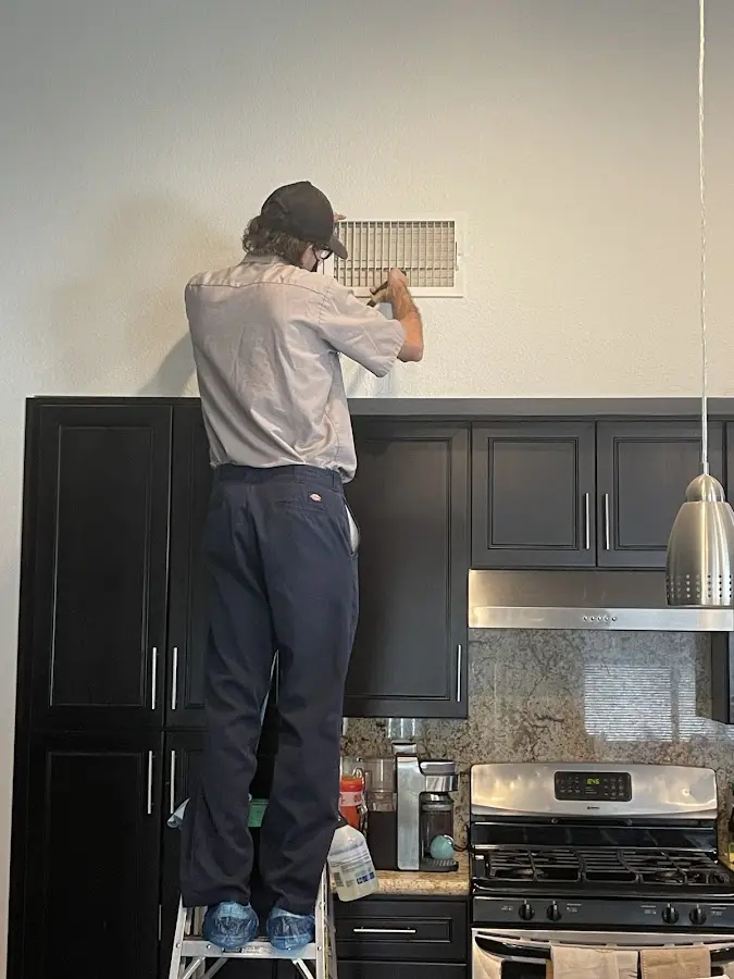 Technician inspecting an air vent during HVAC service in Slinger
